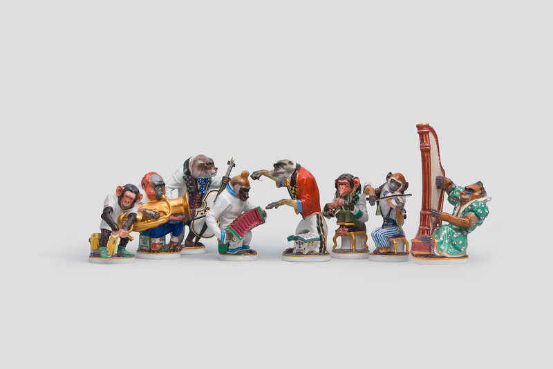 Objektabbildung zoomen Acht nebeneinander aufgestellte Porzellanfiguren, die Affen mit unterschiedlichen Instrumenten beziehungsweise einen Dirigenten darstellen.