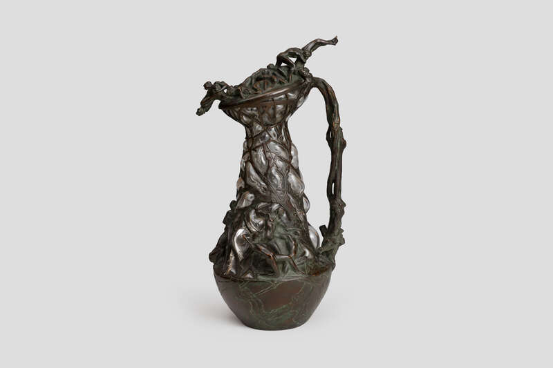 Objektabbildung zoomen Vase aus Bronze mit Dekor aus plastisch modellierten Figuren. Der Glaskörper ist hineingeblasen.