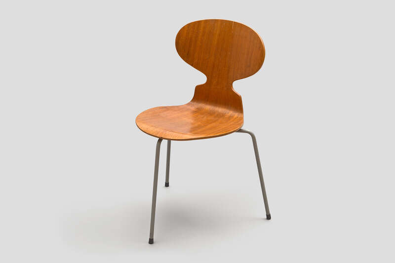 Objektabbildung zoomen Stuhl mit drei dünnen und gebogenen Stahlrohrbeinen. Die Sitzfläche und die Rückenlehne sind aus einem Stück Sperrholz, das zugeschnitten und gebogen wurde.