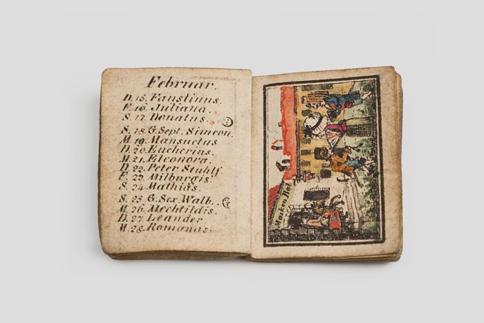 Objektabbildung zoomen Aufgeschlagenes Buch. Auf der linken Seite befindet sich Text, auf der rechten Seite ein Bild mit einer Figurendarstellung.