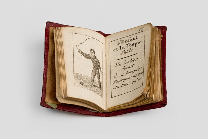 Objektabbildung zoomen Aufgeschlagenes Buch. Auf der linken Seite befindet sich die Darstellung eines Kindes, das mit einem Kreisel spielt, auf der rechten Seite steht Text.
